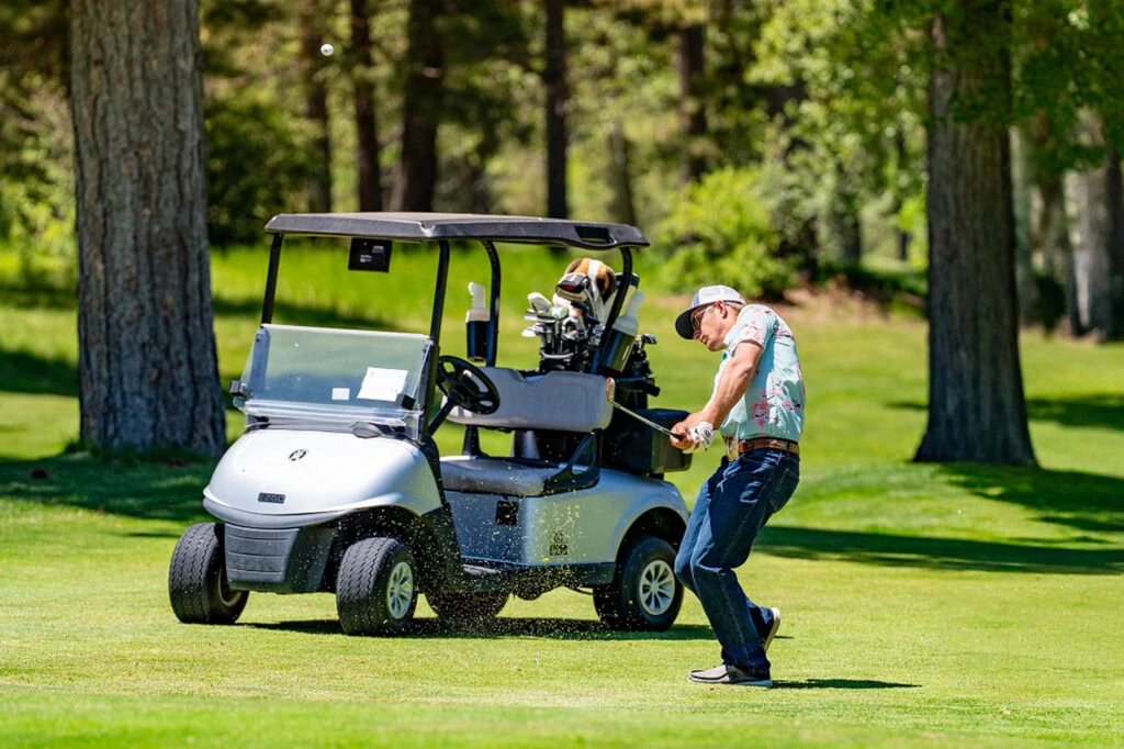 Man hitting golf ball near golf cart at Running Y Resort in beautiful outdoor setting.