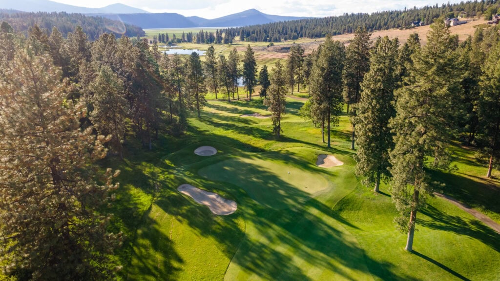 Aerial view of a lush golf course surrounded by trees and mountains in the distance.